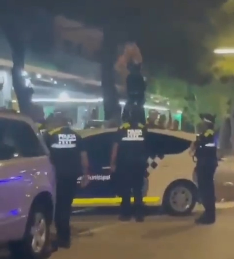 Una mujer baila encima de un coche de policía mientras los agentes esperan a que termine.