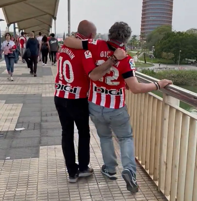 Dos aficionados del Athletic se desplazan con dificultades mientras un sevillano les pone banda sonora.