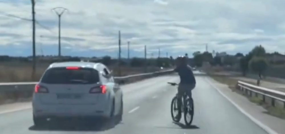 Un ciclista trata de impedir que los coches le adelanten
