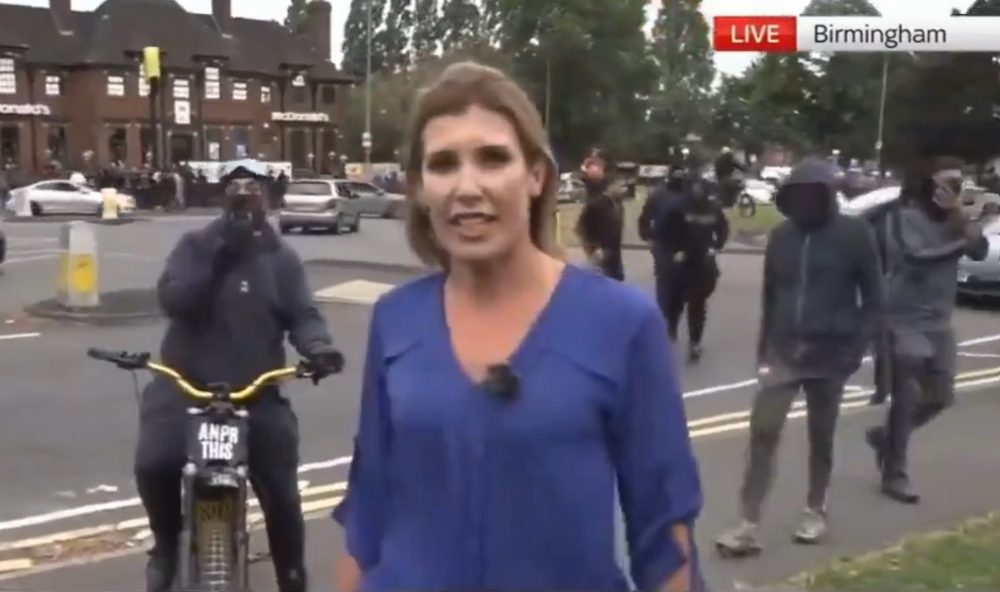 Envían a una periodista a desmentir que los musulmanes la están liando en Inglaterra y aparece un grupo en directo diciendo que paren de grabar haciendo gestos de disparos.