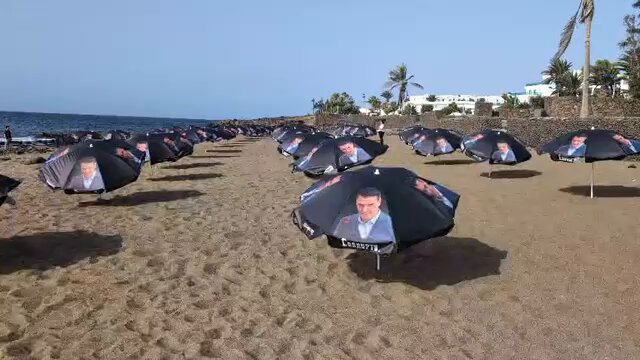 Hazte Oír llena la playa de La Mareta de sombrillas con la cara de Sánchez y la palabra “corrupto”.